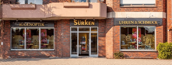 Fassade eines Optiker- und Juweliergeschäfts mit Schaufenstern für Uhren, Schmuck und Brillen.